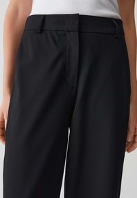 Pantalon noir avec une texture lisse, doté d'une taille classique et d'une fermeture éclair cachée. Le design est ajusté avec une coupe droite.