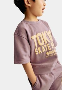 Sudadera de manga corta en color lavanda con estampado amarillo de "TOKYO SKATE PARK". Tejido suave, corte relajado, cuello acanalado, combinada con pantalones a juego.