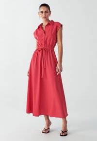 Rød, ærmeløs, knap-op maxi kjole med indsnævret talje og bånddetalje. Glat stof, afslappet pasform, parret med sorte flip-flops.