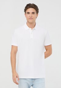 Polo shirt bianca in cotone leggero con colletto classico, dotata di una patta con tre bottoni e maniche corte. Texture liscia, vestibilità rilassata.