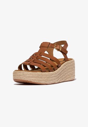 Sandalias de cuña de cuero marrón con tiras cruzadas, plataforma de yute tejido y correa ajustable en el tobillo con detalle de hebilla dorada.