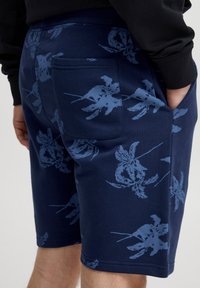 Mornarske kratke hlače z modrim botaničnim tiskom, narejene iz mehke tkanine. Imajo elastičen pas in zadnji žep za shranjevanje.