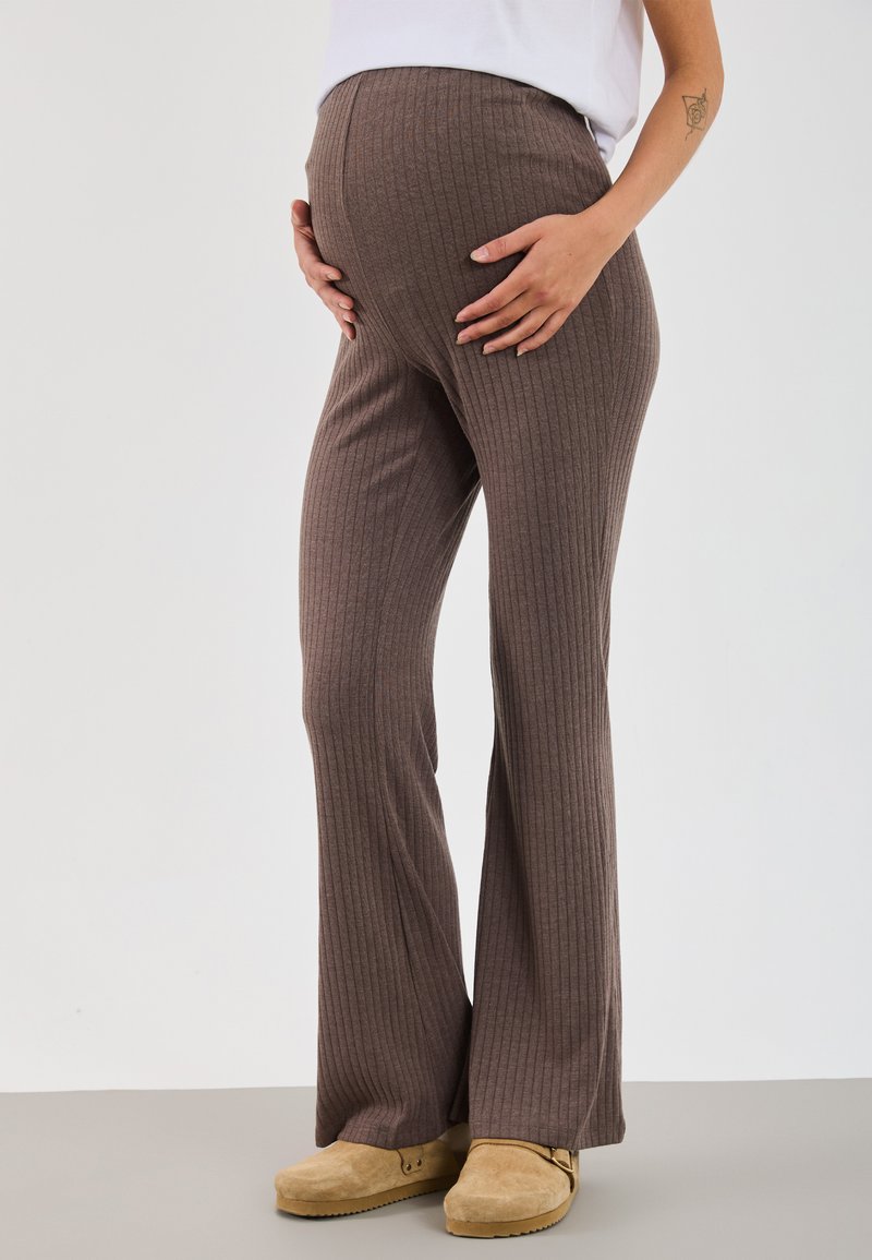 Brown ribbed maternity pants with a fitted waist and flared legs, made of soft fabric, paired with light tan clogs.