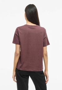 Bordowa bawełniana koszulka z krótkimi rękawami, okrągłym dekoltem i luźnym krojem, przedstawiona z tyłu na jednolitym białym tle.