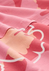 Textile with a pink background featuring abstract shapes in lighter pink and white, showcasing smooth cotton fabric and stitched edges.