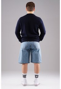 Navy sweater, light blue denim shorts, white socks with black text, and white sneakers. Focus on casual streetwear style and comfort.