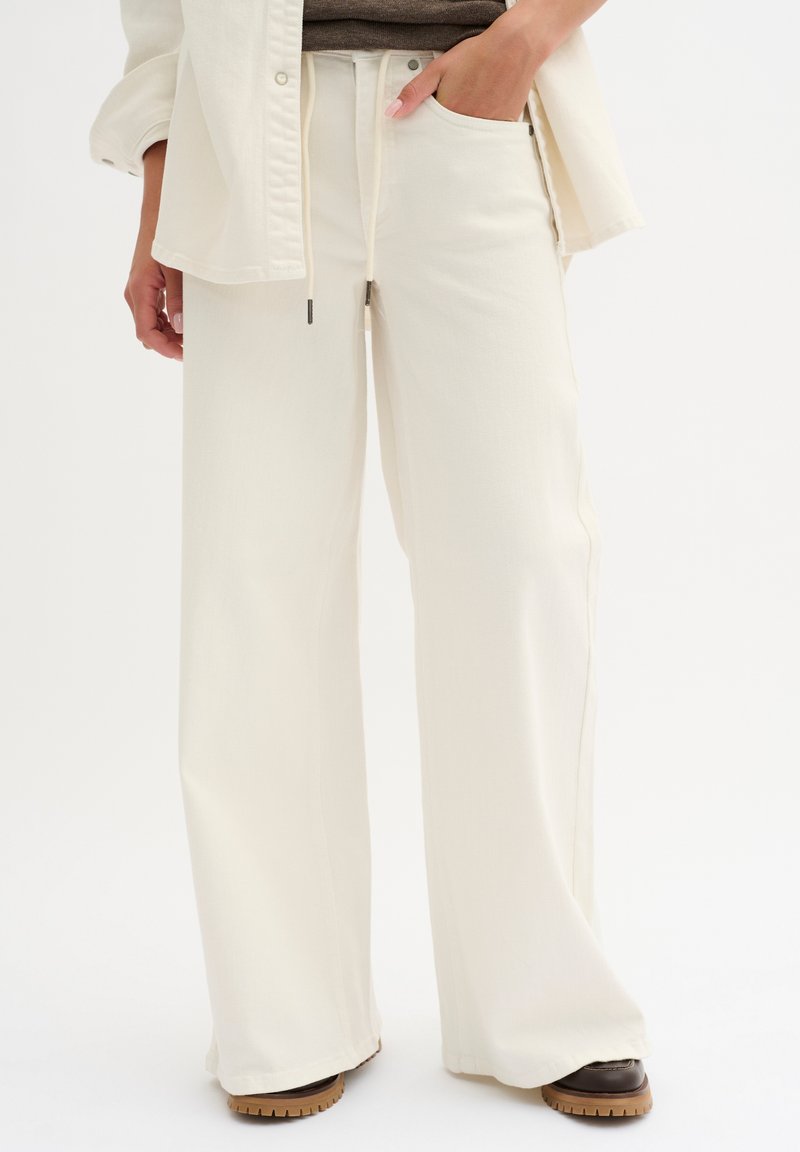 Pantaloni a gamba larga color avorio realizzati in tessuto morbido, con vita regolabile e tasche laterali. L'orlo è leggermente svasato, completando la vestibilità comoda.