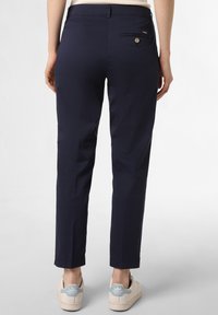 Marineblaue Hose mit schlankem Schnitt, ausgestattet mit einer Gesäßtasche mit Knopfverschluss und einem flachen Bund, kombiniert mit weißen Turnschuhen.