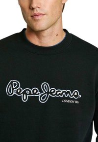 Sudadera negra con un logo bordado en blanco de "Pepe Jeans" y el texto "LONDON W1", con un cuello acanalado y una textura suave.