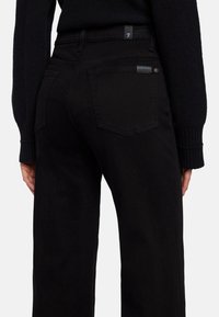 Los jeans negros presentan un diseño de pierna recta con una cintura alta, confeccionados en denim suave. Incluyen dos bolsillos traseros y un branding mínimo en la cinturilla.