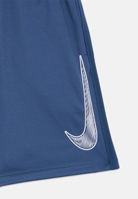 Modré športové šortky s bielym pruhovaným logom Nike swoosh na dolnom pravom boku.