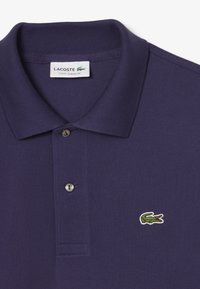 Marinblå polo skjorta med krage, prydd med en liten broderad grön krokodil-logotyp på vänster sida och två knappar vid placket.