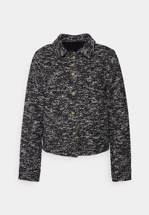 Černobílé tečkované sako s límečkem, knoflíkovým zapínáním a dlouhými rukávy, vyrobené z tkaniny s texturovaným vzhledem.