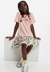 Rosa bomull t-shirt med broderade accenter, i kombination med en knälång vit kjol med färgglada blommönster och bokstavsmönster. Silverfärgade sneakers.