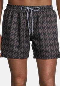 Swim trunks in black with a geometric gray pattern, featuring an elastic waistband and a drawstring closure in contrasting white.