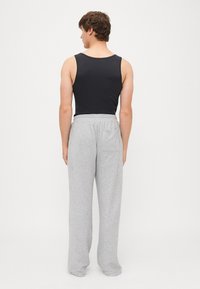 Schwarzes ärmelloses Tanktop kombiniert mit hellgrauen, locker sitzenden Sweatpants. Die Hose hat einen elastischen Bund und eine Gesäßtasche.