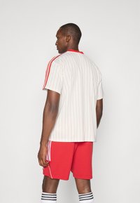 Bílé sportovní tričko s červenými pruhy a límečkem, doplněné červenými šortkami. Šortky mají bílé detaily; ponožky jsou pruhované černobíle.