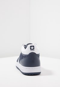 Námornické a bílé vysoké tenisky s hladkým koženým svrškem, polstrovaným límcem a gumovou podešví s texturovanou trakční vrstvou. Logo Converse na patě.