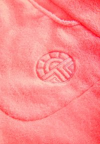 Rosa Plüschstoff mit einem runden Logo, das geometrische Muster zeigt, verziert mit einer geprägten Textur und einem weichen, samtigen Finish.