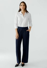 White button-up shirt with rolled sleeves, paired with dark navy wide-leg trousers featuring a smooth waistband and two side pockets.