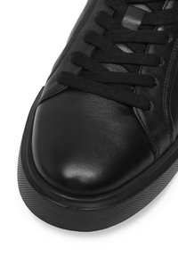 Čierne kožené tenisky s okrúhlou špičkou, plochým zaväzovaním a štruktúrovanou podrážkou s jemným prúžkovaným vzorom pozdĺž okraja.