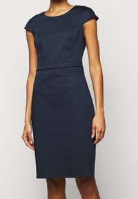 Robe ajustée bleu marine avec des manches courtes, un col rond et un détail de couture horizontal à la taille. Tissu lisse avec une silhouette structurée.