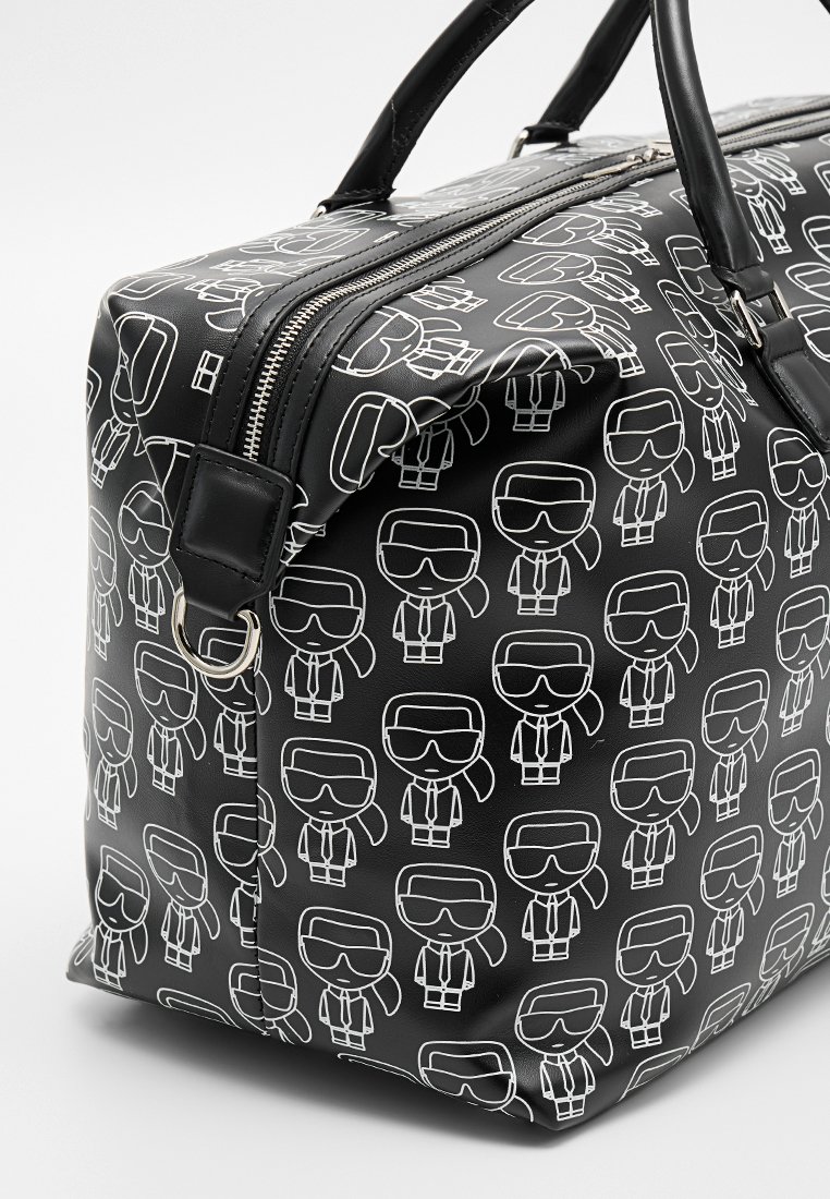 Bolso de viaje sintético negro con figuras de dibujos animados blancas que llevan gafas de sol y trajes, con dos asas negras y una cremallera plateada.