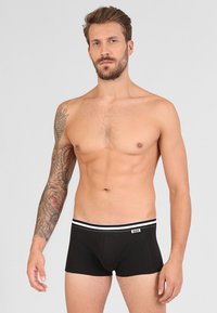Čierne boxerky s bielym elastickým pásom, s logom. Tkanina je hladká a priliehajúca, zvýrazňujúca postavu nositeľa.
