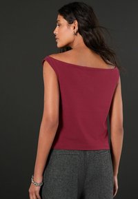 Bordo bezdelīgs tops ar plašu kakla izgriezumu, izgatavots no gludas auduma. Tam ir īsāks dizains, un tas ir saskaņots ar teksturētām pelēkām biksēm.