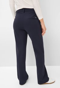 Pantalons larges bleu marine en tissu lisse, avec une poche arrière et une taille ajustée, associés à des baskets blanches.