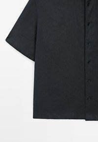 Camicia a maniche corte di colore grigio scuro, realizzata in lino con una superficie texturizzata e colletto classico, dotata di bottoni neri.