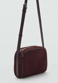 Sac en cuir suédé bourgogne avec une bandoulière en cuir lisse, de forme rectangulaire, fermeture éclair et détails de couture minimalistes.