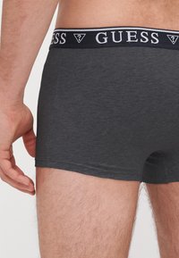 Boxeri scurți gri închis, cu un elastic negru și alb inscripționat cu "GUESS", fabricați din bumbac moale și având un design ajustat.
