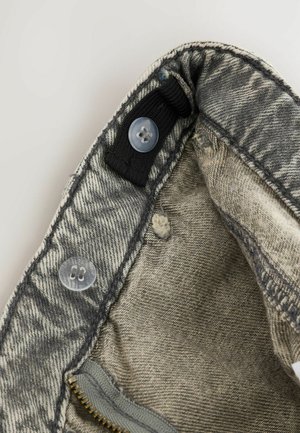 Inner waistband of gray denim jeans showing adjustable black elastic band with clear buttons and a partially visible zipper.