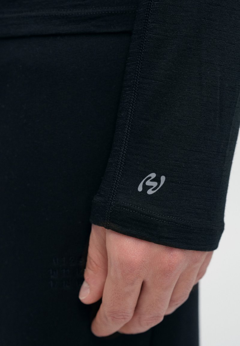 Schwarzes, langärmeliges Oberteil aus elastischem Stoff mit figurbetontem Design und grauem Logoakzent auf dem Ärmel. Nahtdetails sind entlang der Kanten sichtbar.