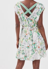 Biała sukienka w kwiaty z zielonymi i pomarańczowymi wzorami, z krótkimi rękawami, elastycznym pasem i zielonymi paskami w kształcie krzyża na plecach.