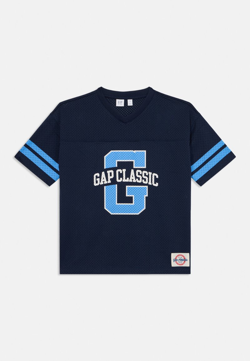 Tumši zils sieta īsās piedurknes T-krekls ar V-veida kakla izgriezumu, ar gaiši ziliem svītrām uz piedurknēm un "GAP CLASSIC" grafiku baltā un zilā krāsā.