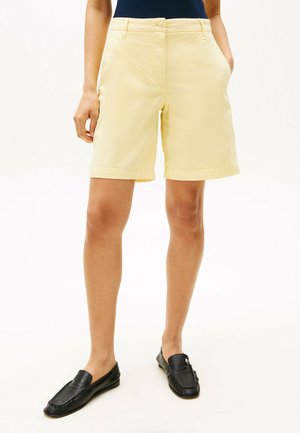 Pantalones cortos de algodón amarillos con una textura suave, puños enrollados y bolsillos laterales, combinados con unos mocasines negros. Cuenta con un cierre frontal de botón.