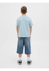 Světle modré bavlněné tričko s krátkým rukávem, spárované s tmavě modrými džínovými šortkami. Tenisky s černobílými akcenty a bílé ponožky.