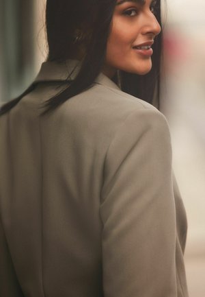 Maßgeschneiderte beige Blazer mit strukturierten Schultern und glattem Stoff. Verfügt über einen Reverskragen und subtile Nähdetails.