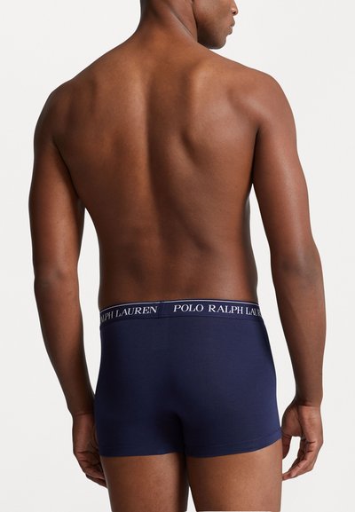 Tamsiai mėlyni šortai su minkšta medžiaga ir kontrastinga juosta, ant kurios baltu textu parašyta "POLO RALPH LAUREN". Sklandus, prigludęs dizainas.