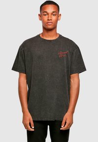 Sort oversized bomulds T-shirt med rund halsudskæring, prydet med røde broderede bogstaver og en let tekstureret, falmet finish.
