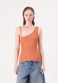 Geribbelde oranje tanktop met asymmetrische halslijn en dunne schouderband, gecombineerd met wijde blauwe spijkerbroek.