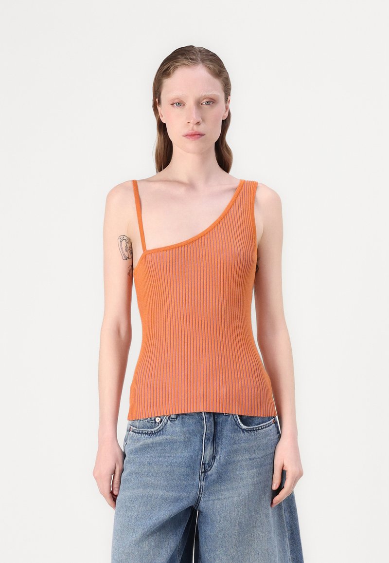Geribbelde oranje tanktop met asymmetrische halslijn en dunne schouderband, gecombineerd met wijde blauwe spijkerbroek.