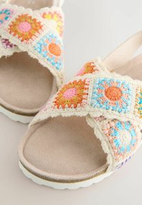 Virksandaler med flerfärgade blommönster, krämfärgade vävda remmar och texturerade sulor. Mjuk innerfoder med en något upphöjd kant.