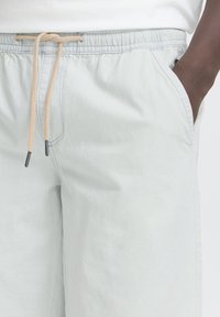 Svetlo sive kratke hlače z elastičnim pasom in bež vrvico za zategovanje, z bočnimi žepek in mehko, gladko teksturo.