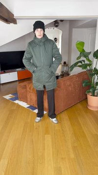Groene, geïsoleerde parka met een rits aan de voorkant, twee zijkanten zakken en een hoge kraag, gedragen over donkere broek en zilveren sneakers.