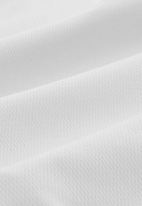 Weißer texturierter Stoff mit einem subtilen Diamantmuster, das eine glatte, leicht glänzende Oberfläche und gefaltete Lagen aufweist, die Schatten erzeugen.