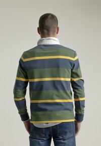 Camisa polo de manga larga con rayas horizontales en verde, azul marino y amarillo. Cuenta con puños acanalados y una capa de camisa blanca con cuello por debajo.