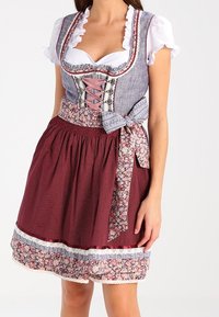 Robe traditionnelle dirndl avec un corsage bleu, un devant à lacets, des manches blanches et une jupe rouge à pois avec des accents floraux et une bordure en dentelle.